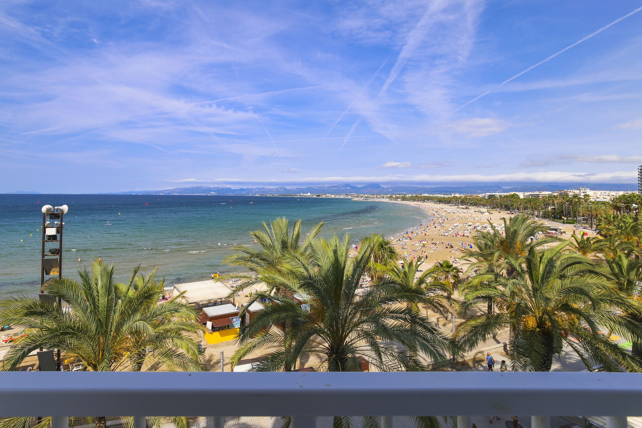 A beach view with palm trees, a lifeguard tower, and a clear sky.