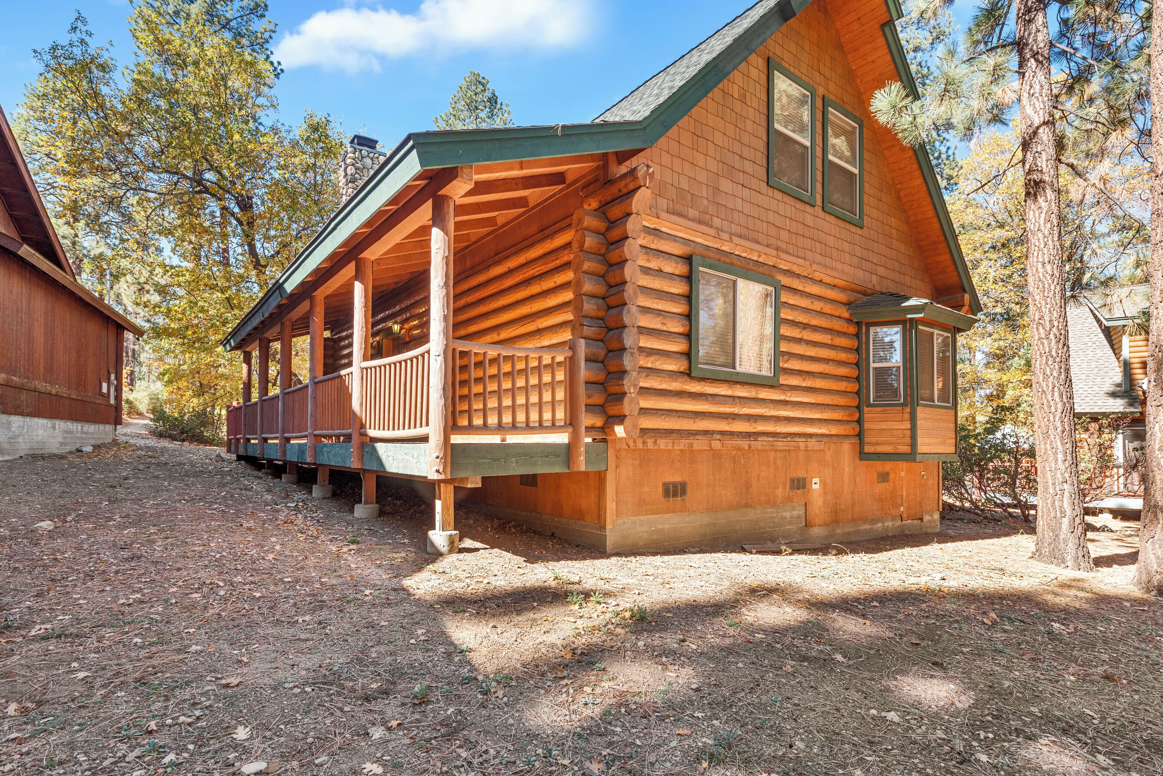 A log cabin with a porch, surrounded by trees.