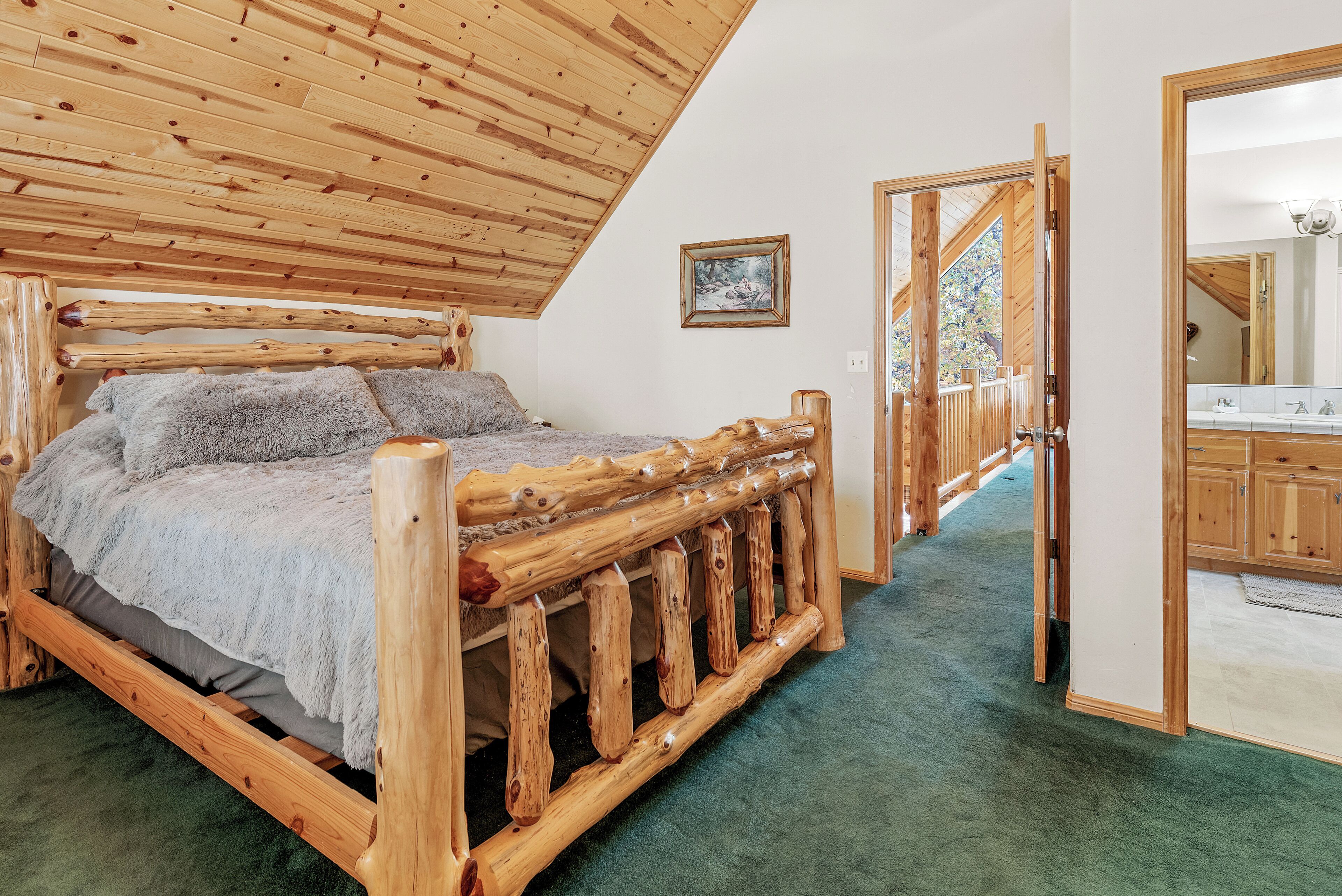 Una cama de madera con alfombra verde, techo de madera y puerta de madera que da a un baño.