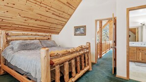 A wooden bed with a green carpet, a wooden ceiling, and a wooden door leading to a bathroom.