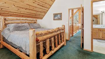 Una cama de madera con alfombra verde, techo de madera y puerta de madera que da a un baño.