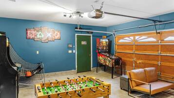 Une pièce avec une table de baby-foot, une table de ping-pong, une porte verte et une porte de garage.