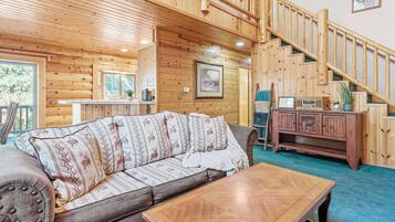 Interior de una cabaña de madera con sofá, una mesa, una escalera y un armario.