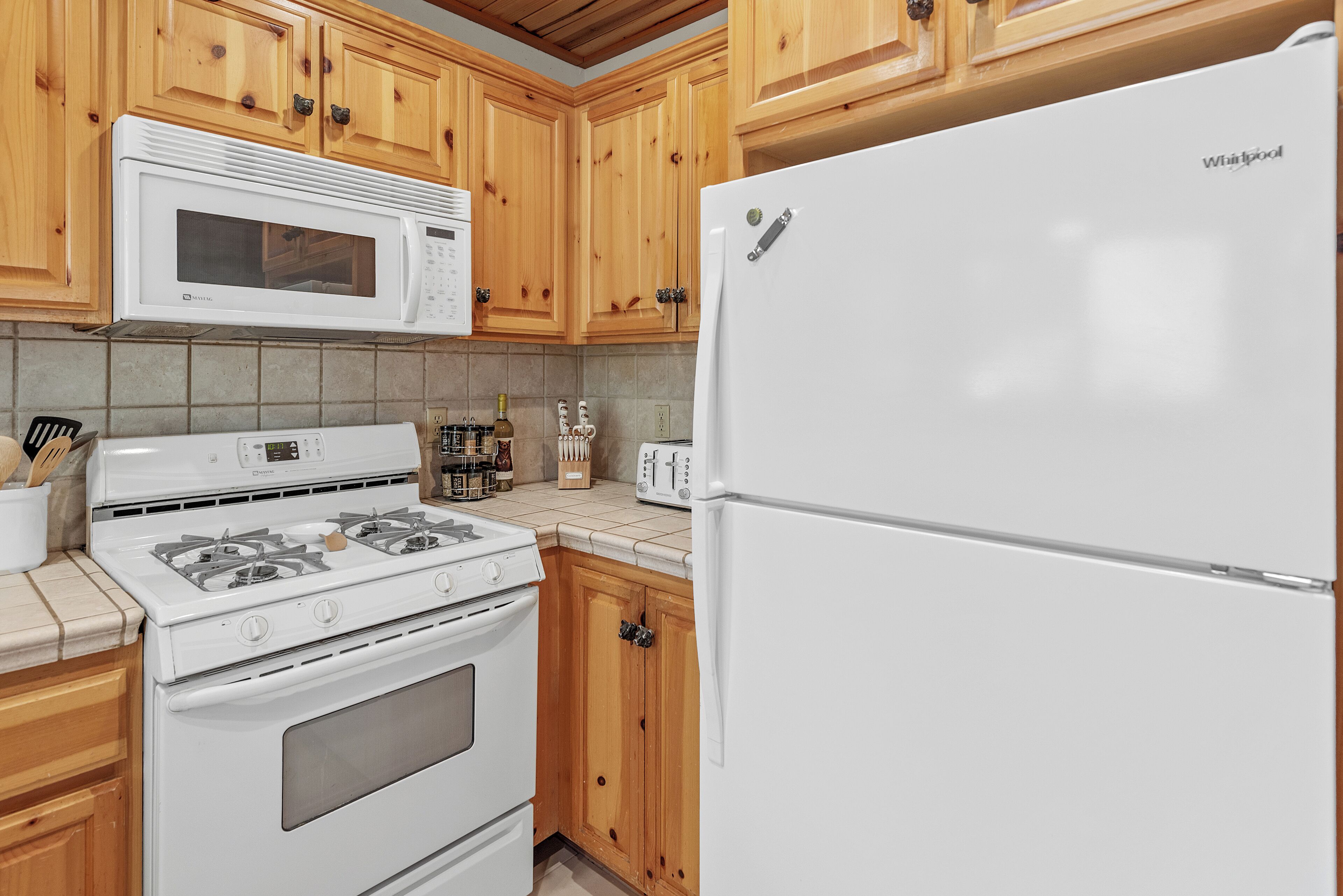 A kitchen with wooden cabinets, a white microwave, a stove, and a refrigerator.