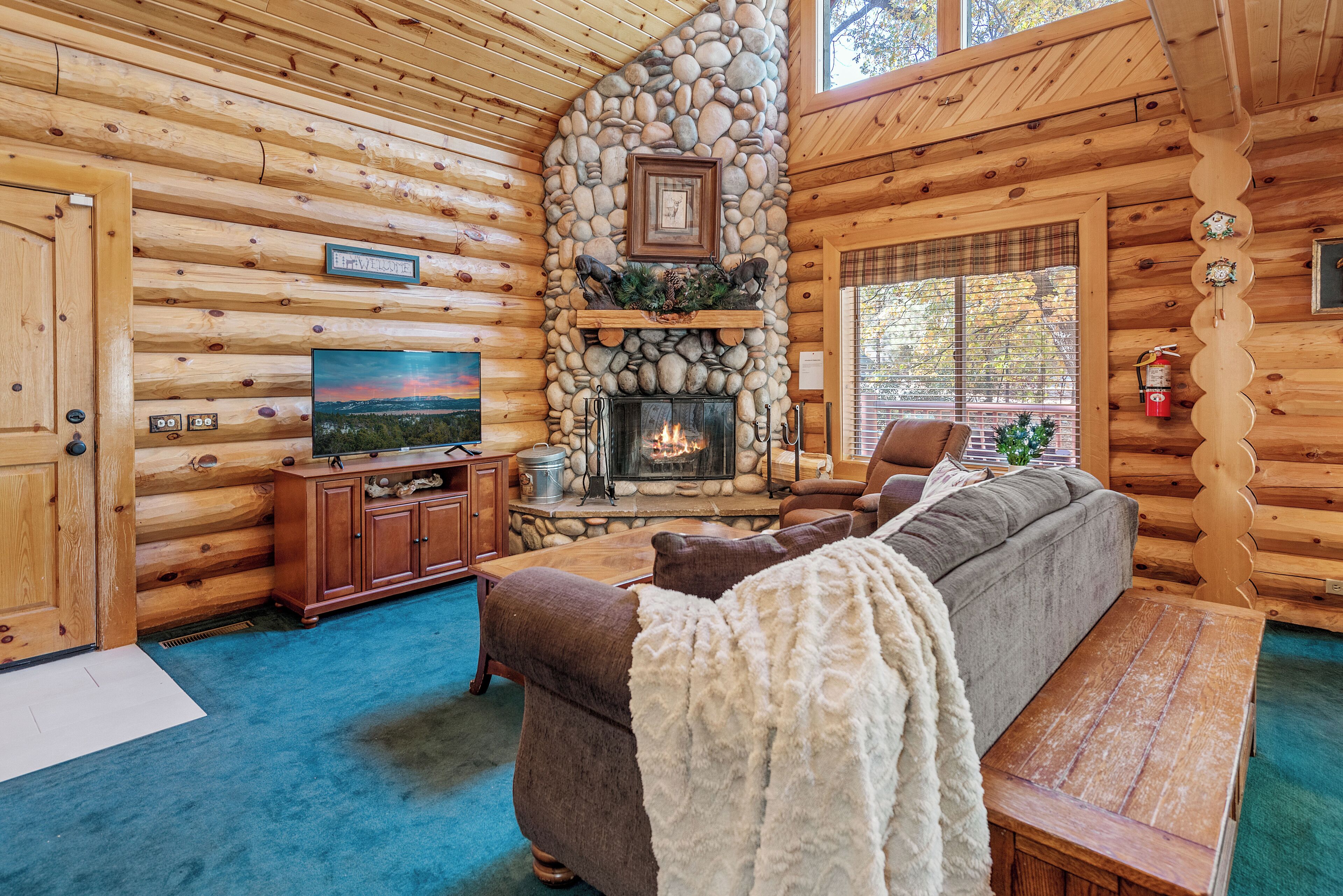 A log cabin interior with a stone fireplace, a television, a sofa, and a wooden bench.