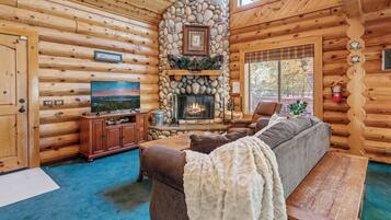 A log cabin interior with a stone fireplace, a television, a sofa, and a wooden bench.