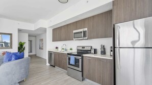 A modern kitchen with stainless steel appliances, wooden cabinets, and a grey sofa in the living area.