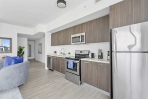 A modern kitchen with stainless steel appliances, wooden cabinets, and a grey sofa in the living area.