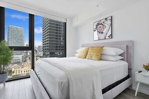 A modern bedroom with a large bed, a city view, and a framed artwork on the wall.