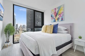 Een moderne slaapkamer met een groot bed, stadszicht en een schilderij aan de muur.