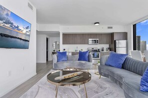 Een moderne woonkamer met een grijze bank, een ronde salontafel en een keuken op de achtergrond.