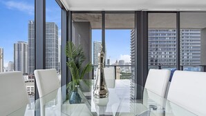 Ein modernes Interieur mit einem Glastisch, weißen Ledersesseln und Blick auf eine Stadtlandschaft durch große Fenster.