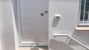 Eine weiße Tür mit kleinem Fenster darüber, einer wandmontierten Leuchte und einem Klingelknopf.