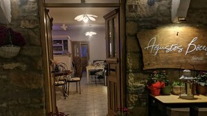 Una entrada de paredes de piedra con una puerta de madera, un área de comedor con una mesa y sillas, y un letrero en la pared con texto.