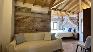 Una habitación acogedora con techo de madera, pared de ladrillo, un sofá blanco grande y una cama con dosel.