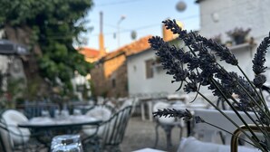 Un área de comedor al aire libre con mesas redondas, vasos de vidrio transparente y un florero con lavanda.