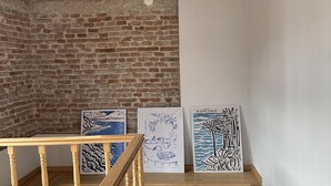 Una escalera de madera junto a un muro de ladrillo y tres obras de arte enmarcadas sobre una estantería.