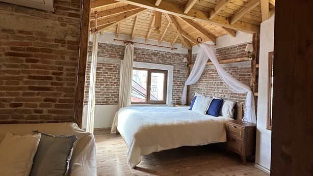 Un dormitorio con techo de madera, pared de ladrillo, cama con almohadas y mesita de noche.