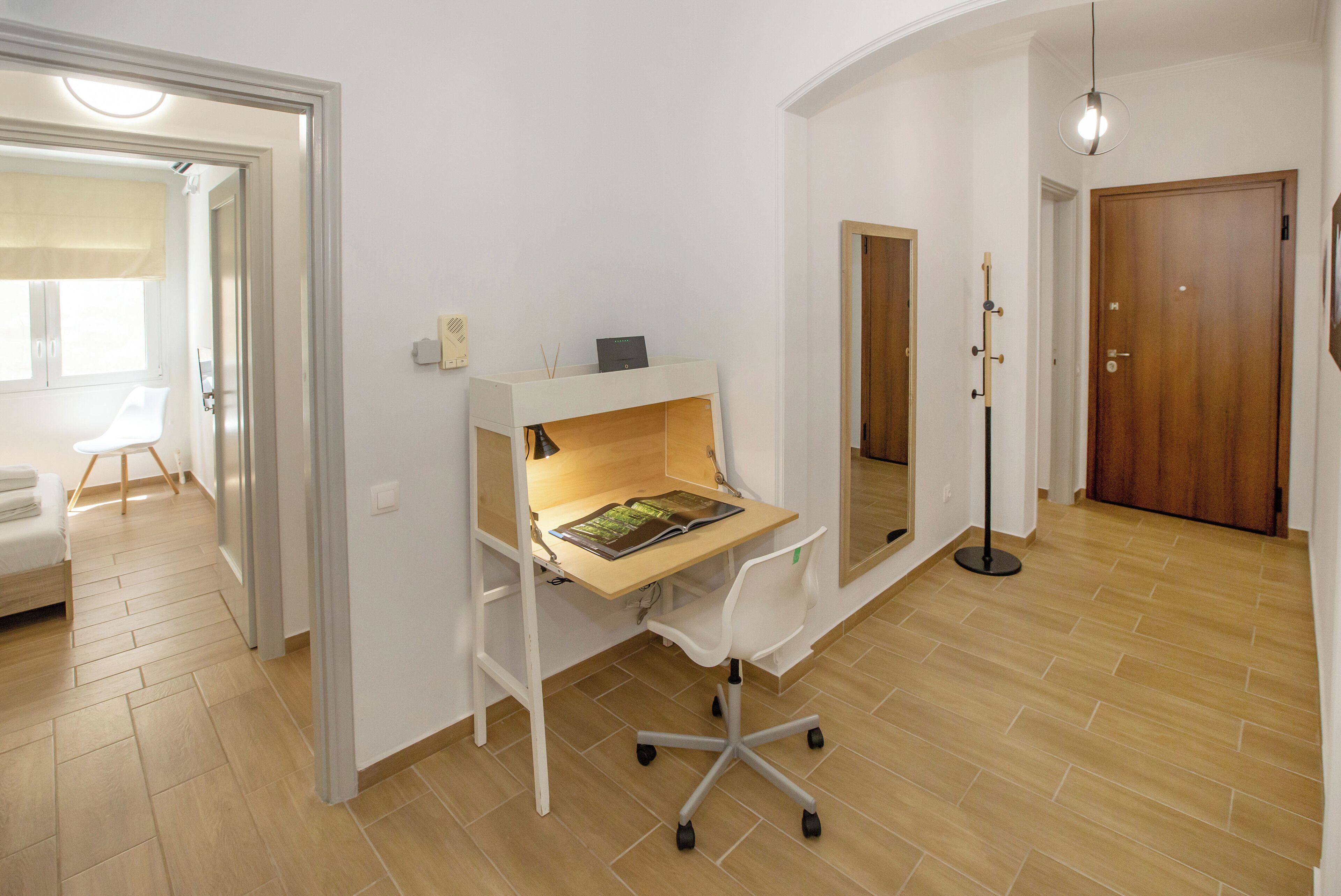 A modern room with a wooden desk and chair, a standing lamp, and a wooden floor.
