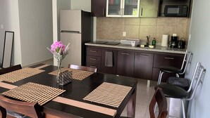 Une cuisine moderne avec des meubles de couleur sombre, un réfrigérateur en acier inoxydable, un four à micro-ondes et un évier. On y trouve une table à manger avec des sets de table et un vase rempli de fleurs.
