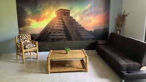Un salon avec une grande fresque représentant une pyramide, une table basse en bois, un canapé et un fauteuil.