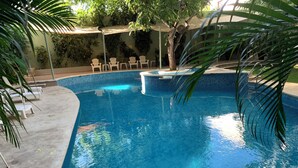 Une piscine d’un bleu éclatant, bordée de carreaux, entourée de chaises longues blanches et d’un palmier.