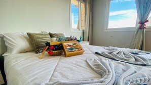 A neatly made bed with a basket of flowers, a tray with a teapot, and a framed picture on a hotel room bed. - COBERTURA 04 Suites - RUA COBERTA  (Gramado)