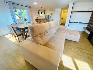 Sala de estar com sofá, mesa de jantar, cadeiras e cozinha com geladeira.