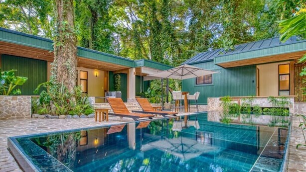 A modern outdoor pool area with a clear pool, lounge chairs, and a covered seating area.