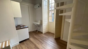 A room with a wooden floor, white walls, a desk with a chair, and a window with a view of buildings outside. - Executive suite (Catania)