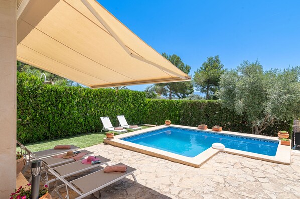 Une piscine rectangulaire bordée d’une terrasse en pierre, entourée de chaises longues et de plantes en pot.