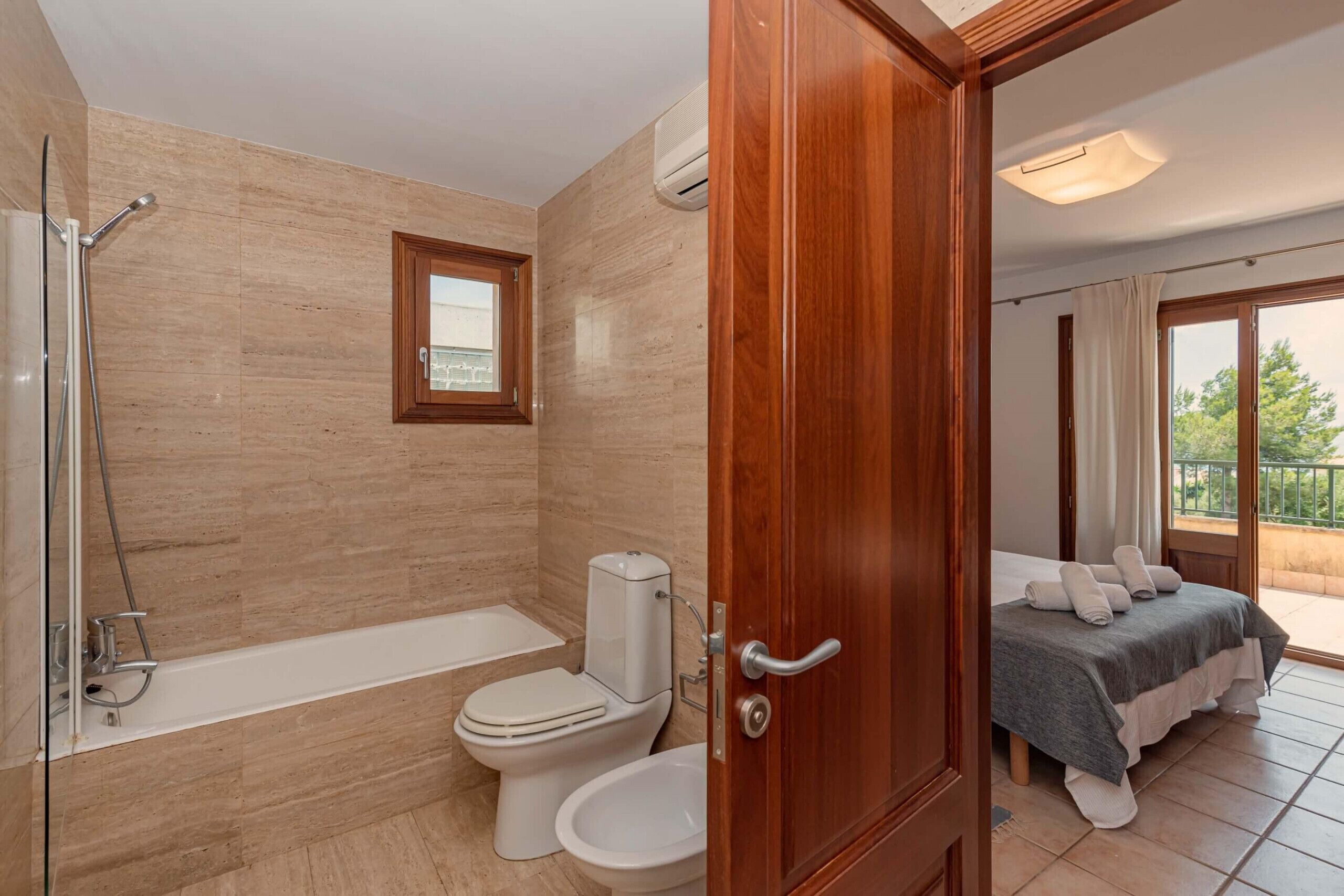 A bathroom with a bathtub, toilet, and bidet, a wooden door, and a balcony with a bed.