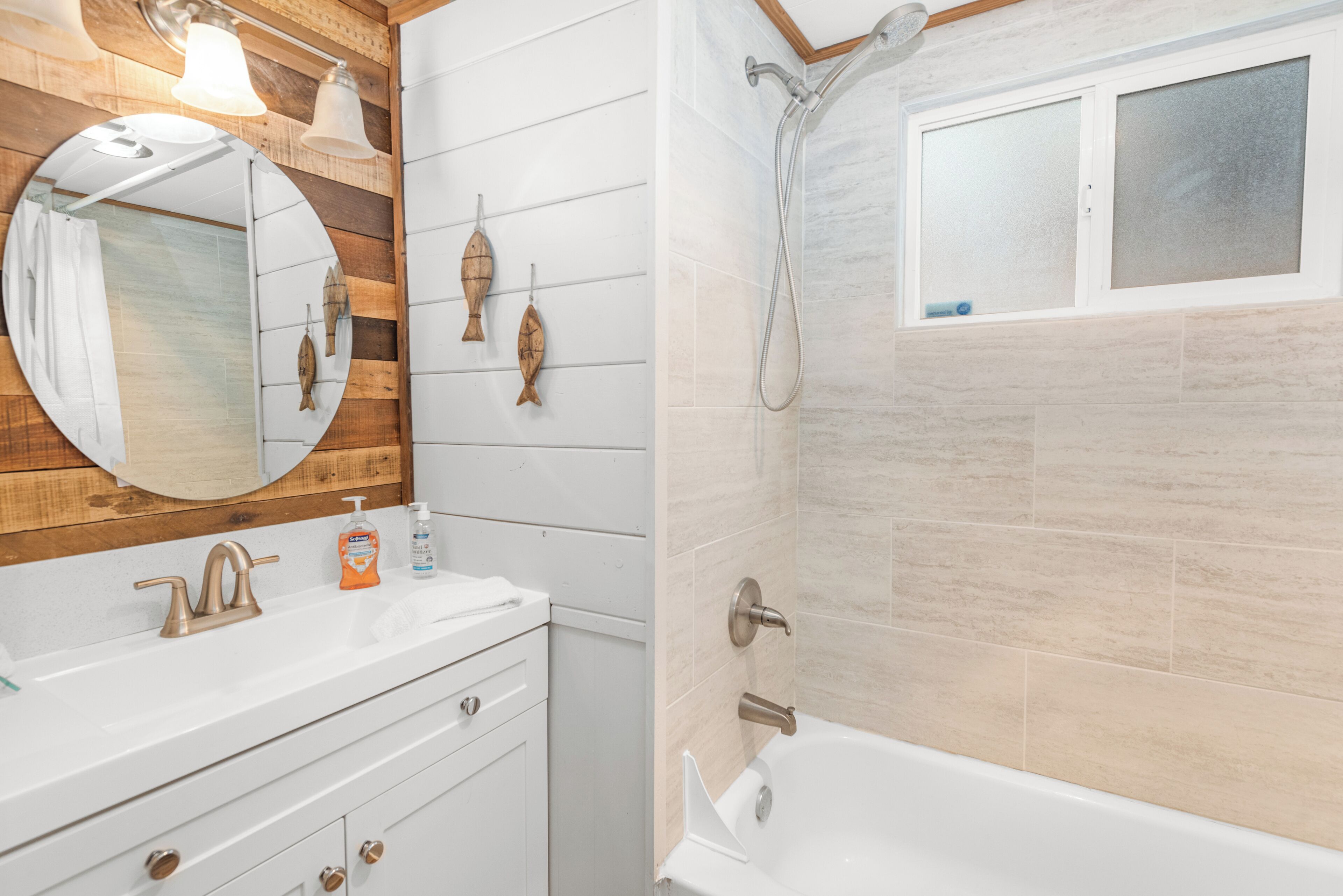 Un baño con tocador de madera, un espejo redondo, bañera y ducha.