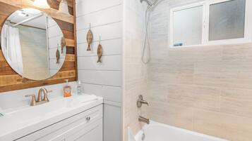 Un baño con tocador de madera, un espejo redondo, bañera y ducha.