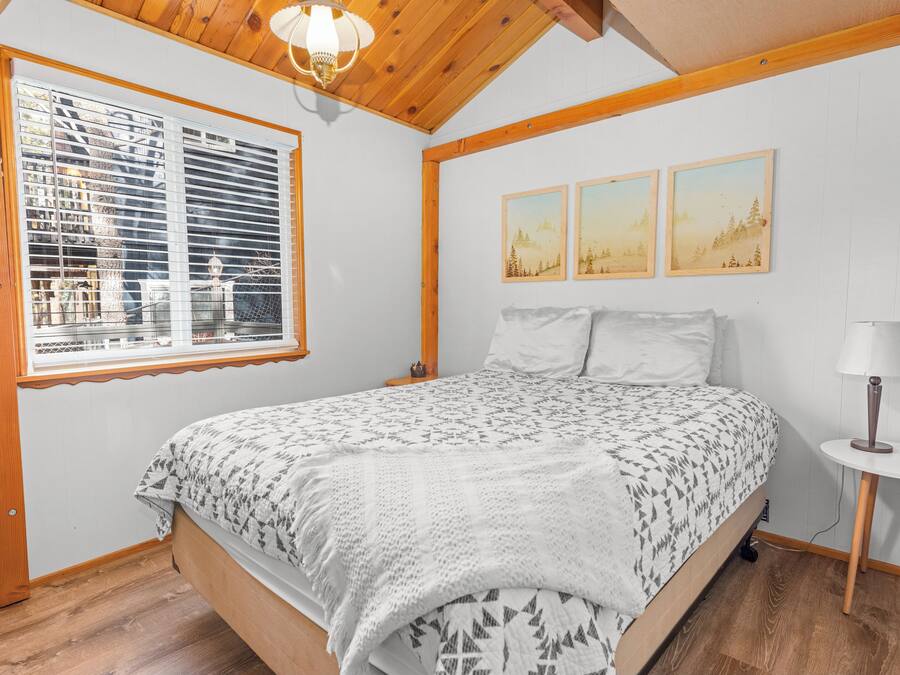 Un dormitorio con cama, ventana con persianas, lámpara y dos cuadros en la pared.