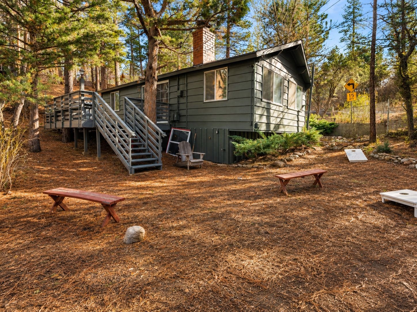 Una cabaña con una escalera que conduce a una terraza, rodeada de árboles y mobiliario exterior.