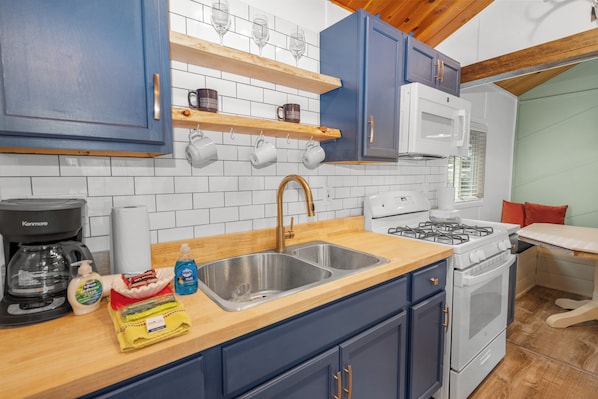 Une cuisine avec des meubles de couleur bleue, un four à micro-ondes blanc, une cuisinière à gaz et des étagères en bois au-dessus de l’évier.