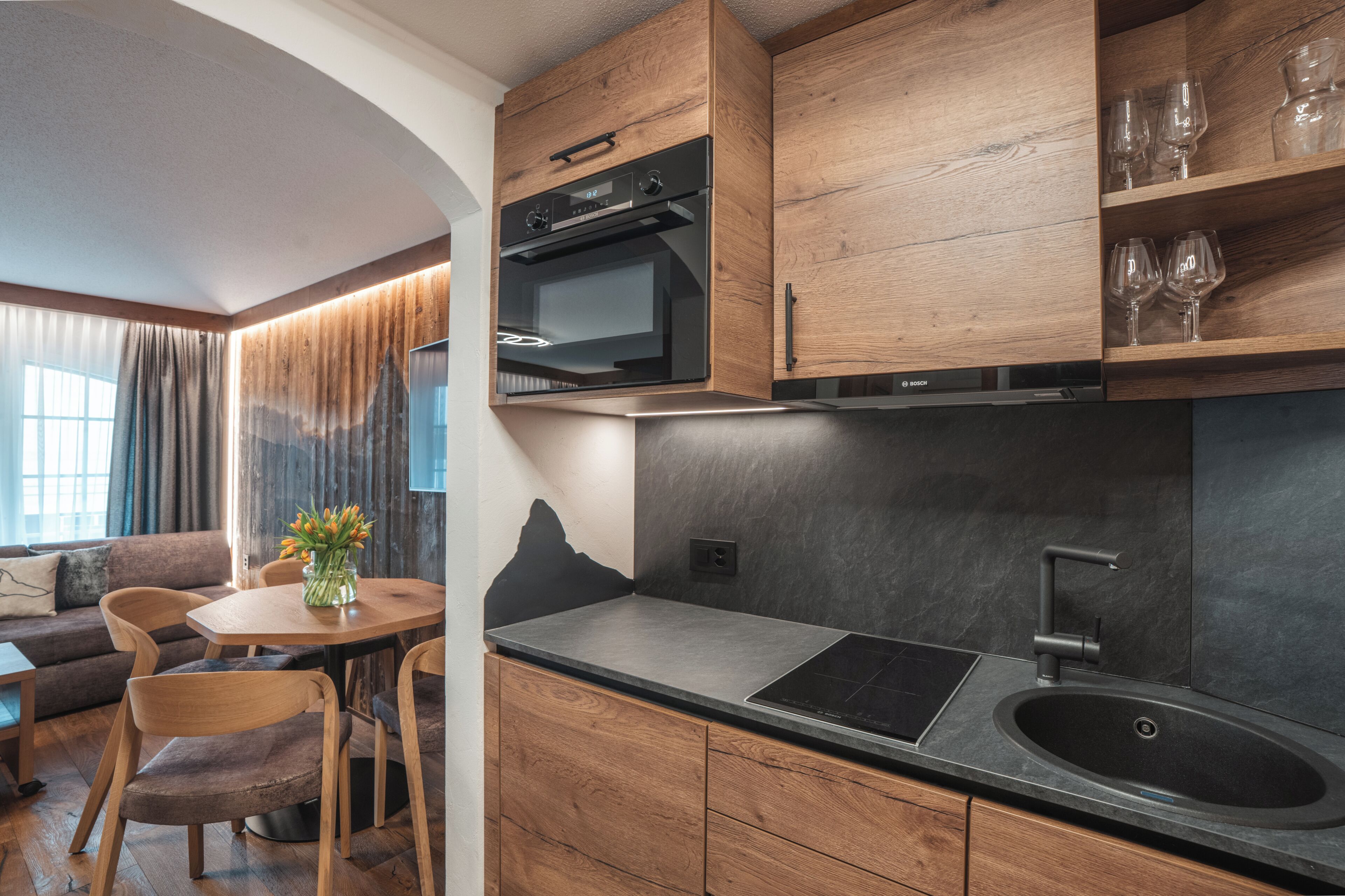 Een moderne keuken met houten kastjes, een ingebouwde oven en een zwart aanrecht.