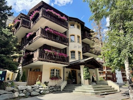 Hotel de vários andares com varandas decoradas com flores, fachada de pedra e entrada convidativa com degraus.