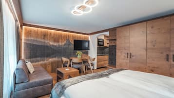 Une chambre d’hôtel moderne équipée d’un lit, d’un canapé, d’une table à manger avec des chaises, d’un téléviseur et d’armoires en bois.