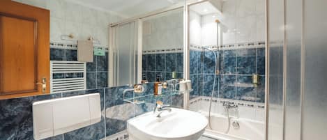 A bathroom with a white sink, a glass shower enclosure, and a wooden cabinet.