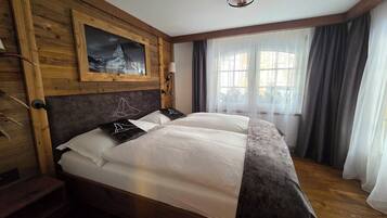 A double bed with white linens, a wooden headboard, and a mountain painting above it.
