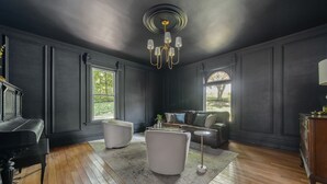 Um quarto com um piano, uma poltrona branca, um sofá e um candelabro.