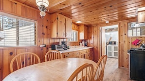 A wooden interior with a round dining table and chairs, a kitchen area with appliances, and a window with blinds. - Boulder Bay Lakefront Getaway (Big Bear Lake)