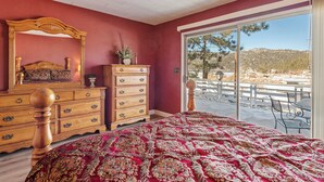 A bedroom with a large bed, wooden dresser, and a mirror. There is a view of a patio with outdoor furniture. - Boulder Bay Lakefront Getaway (Big Bear Lake)