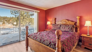 A bedroom with a large bed, wooden headboard, two bedside tables with lamps, and a sliding glass door leading to a balcony. - Boulder Bay Lakefront Getaway (Big Bear Lake)