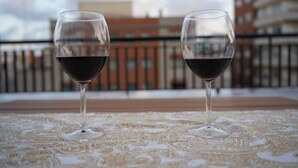 Duas taças de vinho sobre uma toalha de mesa estampada, com uma paisagem urbana ao fundo.