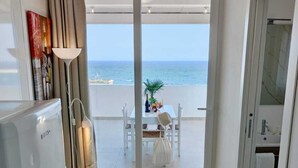 Una cocina moderna con refrigerador, un comedor con mesa y sillas, y un ventanal corredizo que da a un balcón con vista al mar.