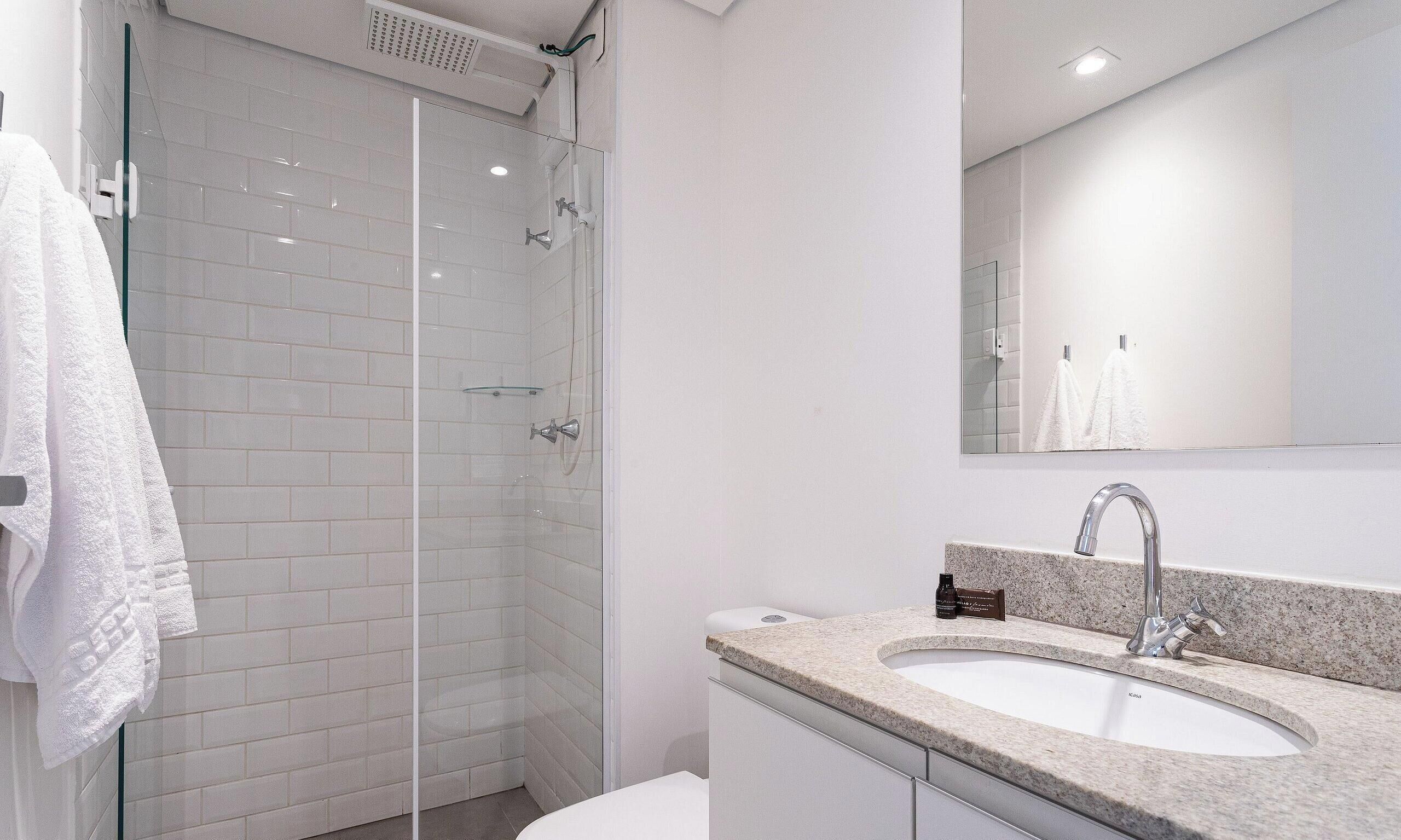Une salle de bain moderne avec une douche à parois de verre, un lavabo doté d’un plan de travail en marbre et un grand miroir au-dessus du lavabo.