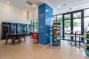 Un interior moderno con un refrigerador marca KIBON, un pilar azul con señalización Smartbreak Petendo, y una zona de estar con mesas y sillas.